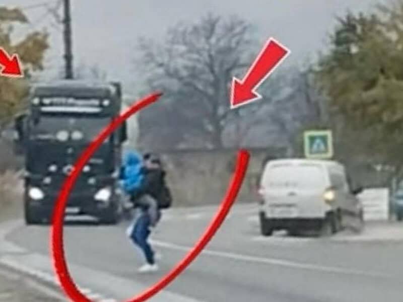 Mamă cu copilul în brațe traversează strada printre autocamioane ignorând siguranța pietonilor