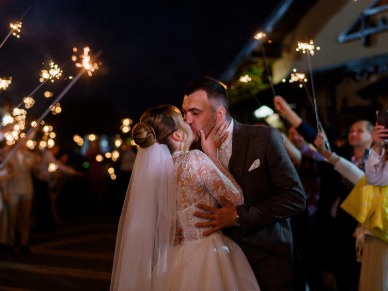 side view beautiful bride bridegroom which hugging kissing each other while guests holding cold sparkles which burning creating glowing arch night ceremony outdoor