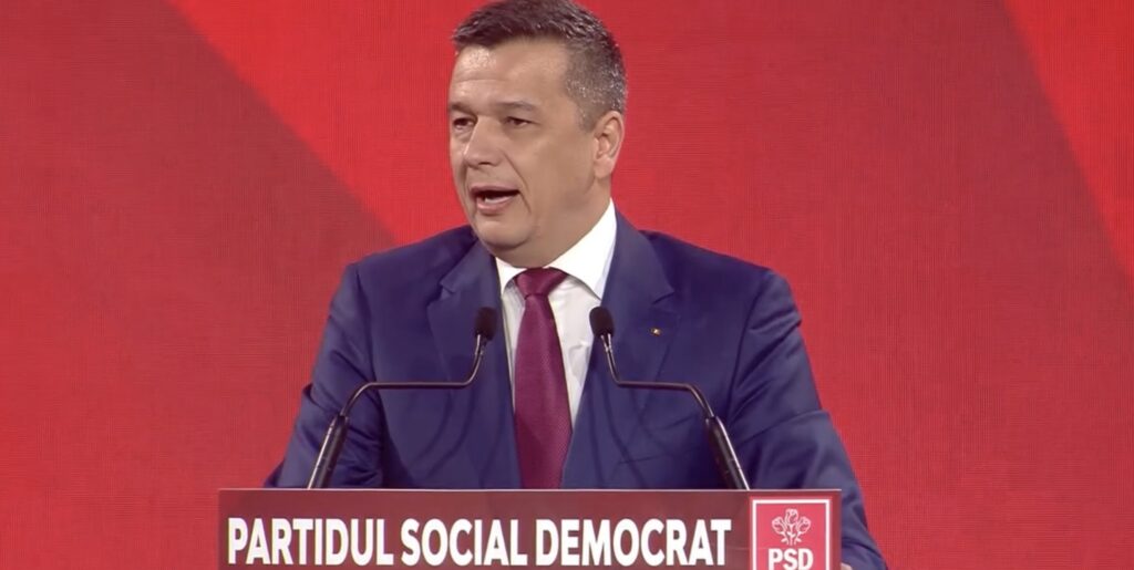sorin grindeanu propune comasarea localitatilor mici pana in martie 2027 Sorin Grindeanu vorbind la pupitru, în fața unui fundal roșu, la un eveniment al Partidului Social Democrat